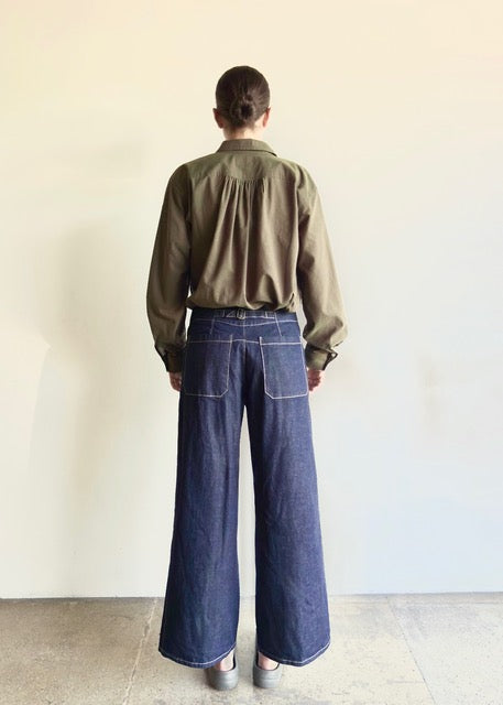 rear view of Person wearing an olive top and Artist Pant indigo jeans on a plain background