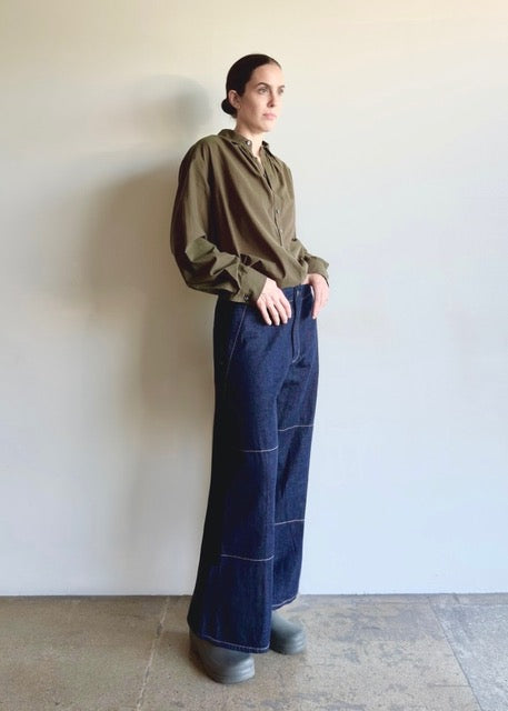 Person wearing an olive button down top and Artist Pant indigo jeans on a plain background