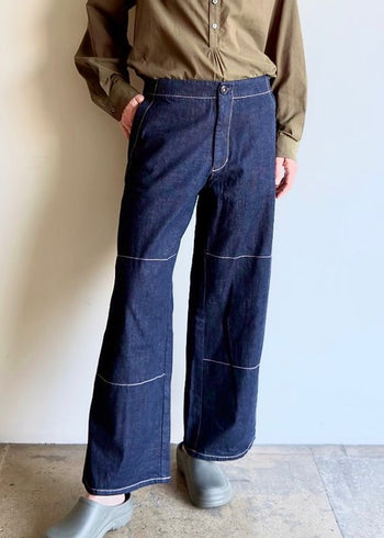 Person wearing an olive button down top and Artist Pant indigo jeans on a plain background
