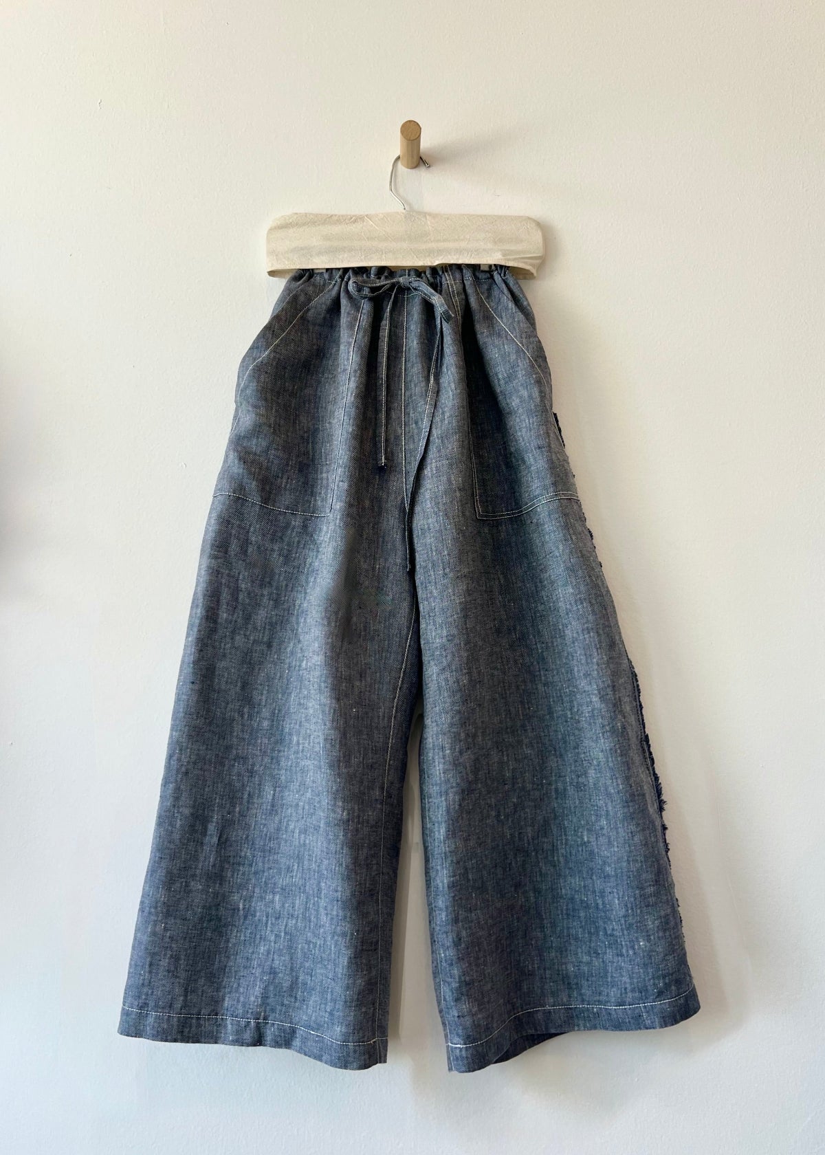 Blue denim color wide-leg pants on a hanger against a white background