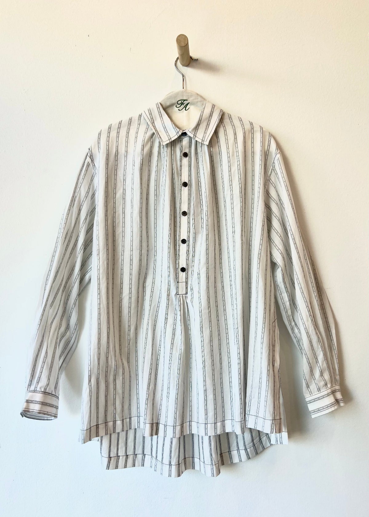 white shirt with gray stripes and buttons hanging against a white wall