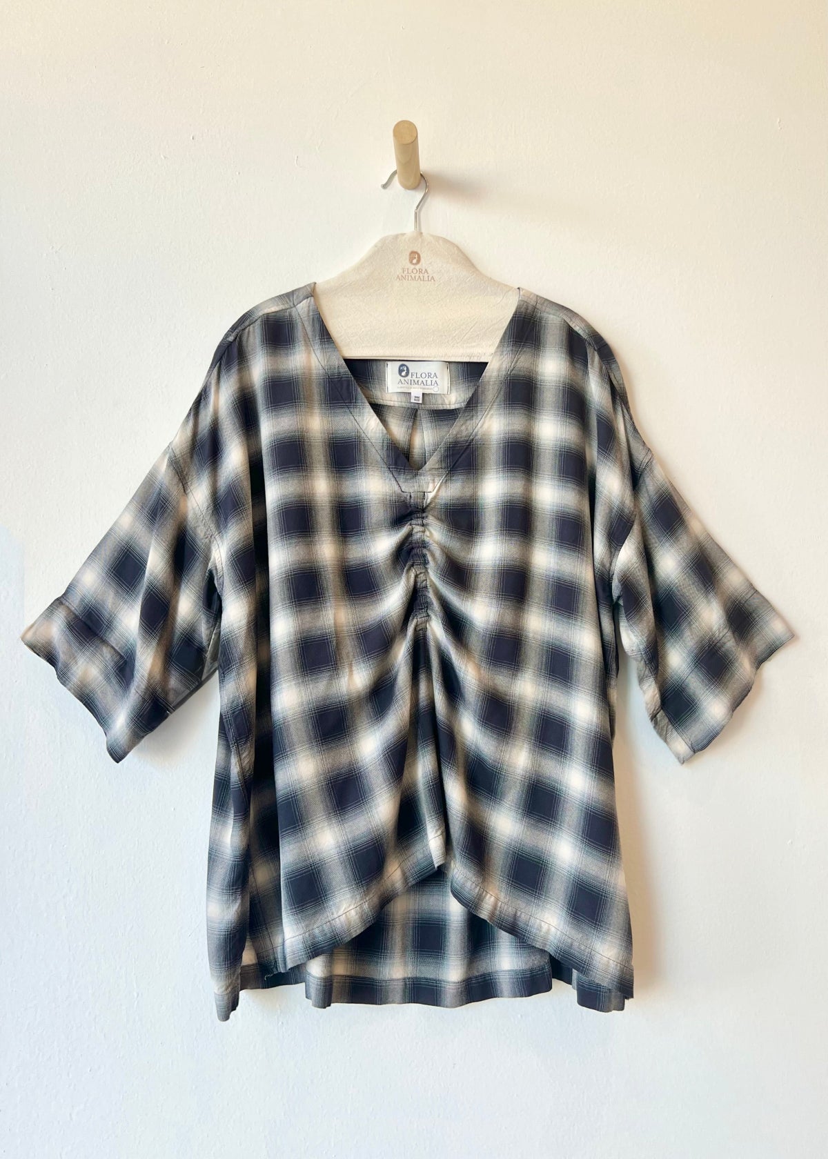 navy and ivory plaid v-neck top hanging against a white wall