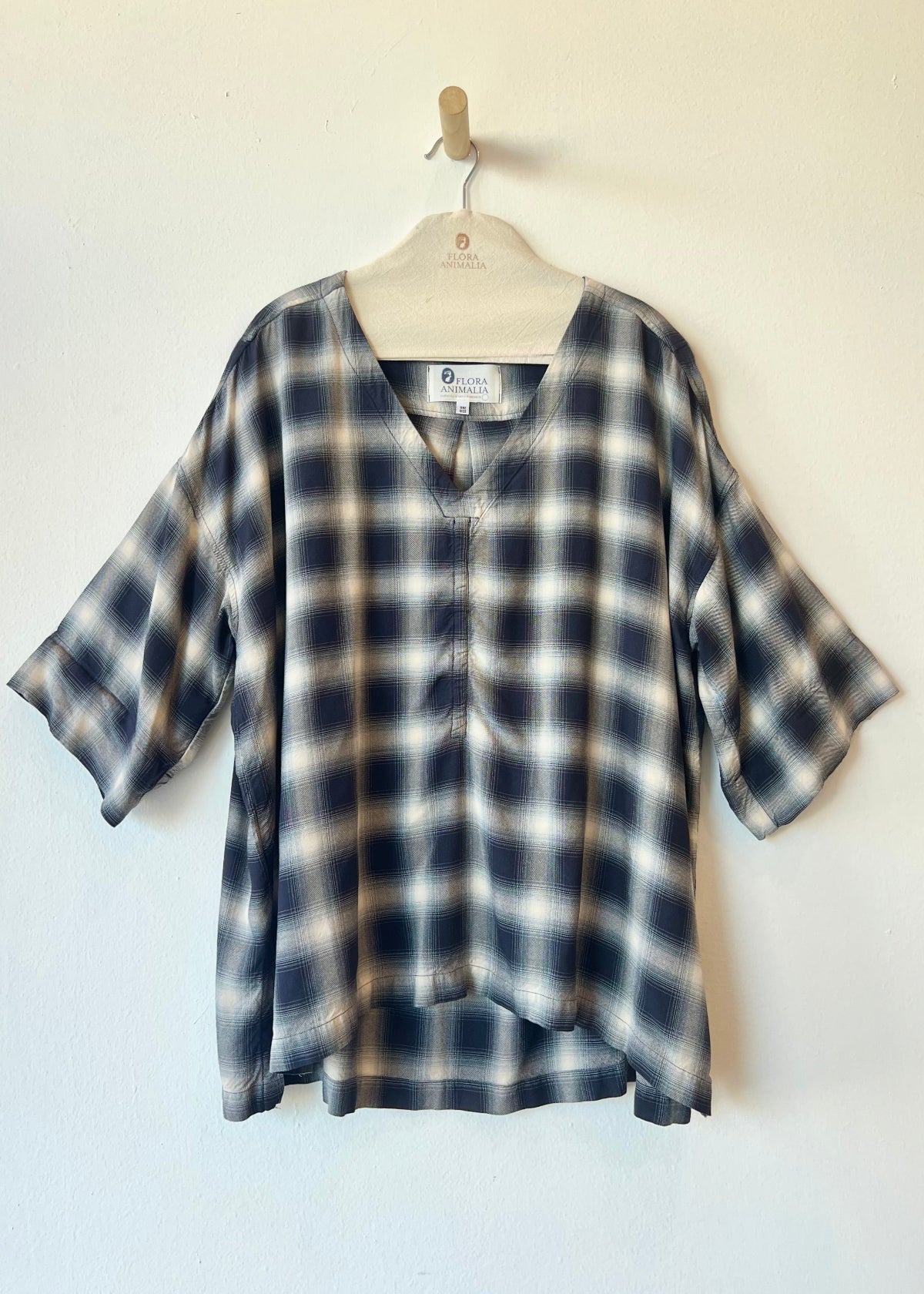 navy and ivory plaid v-neck top hanging against a white wall
