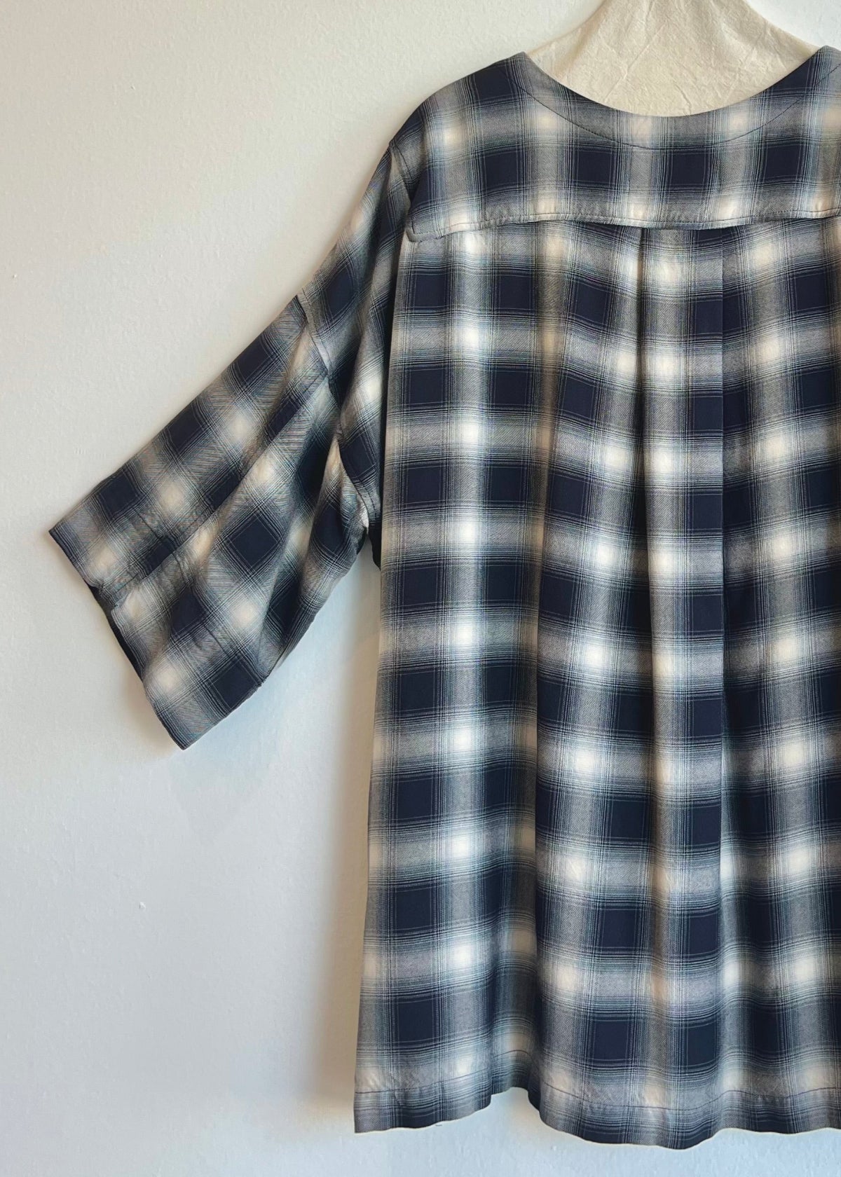 Rear view of plaid top on a hanger against a white background