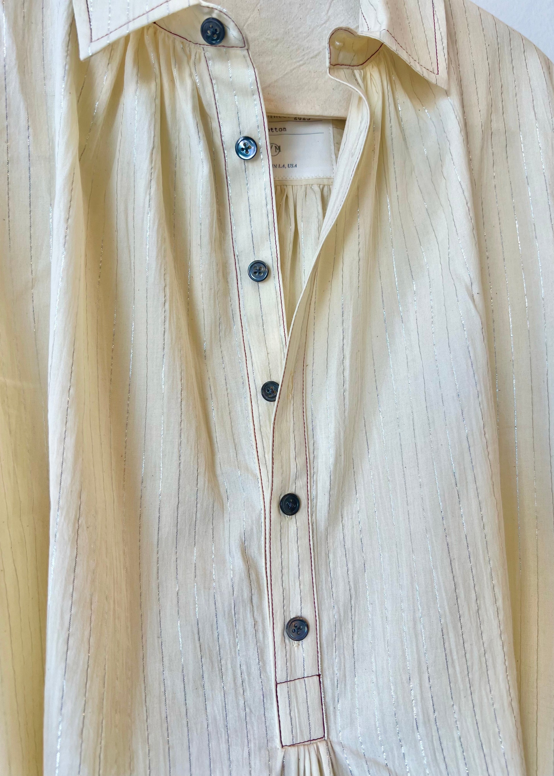 Beige button-up shirt with thin silver stripes and  black buttons on a light background