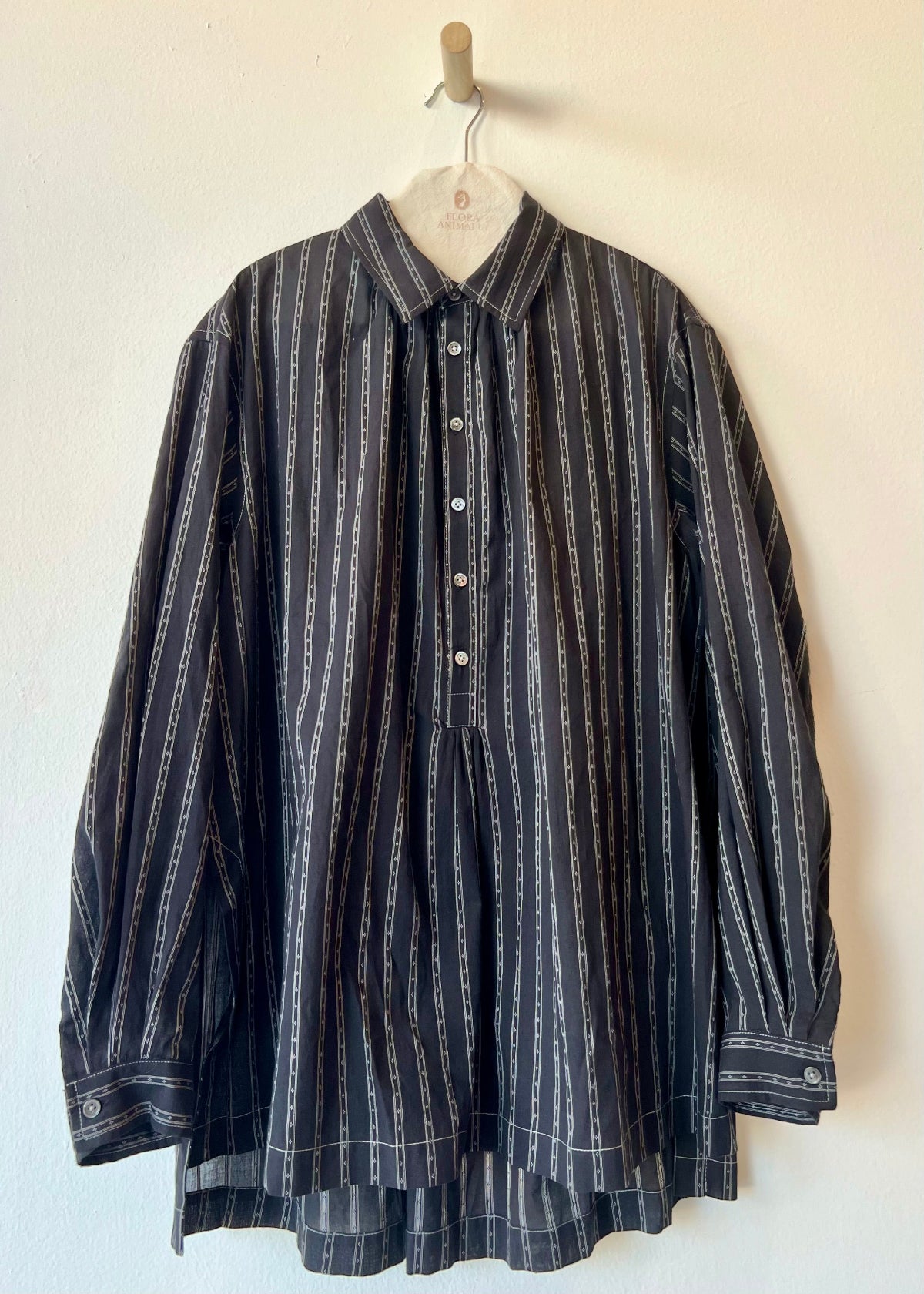 white shirt with gray stripes and buttons hanging against a white wall