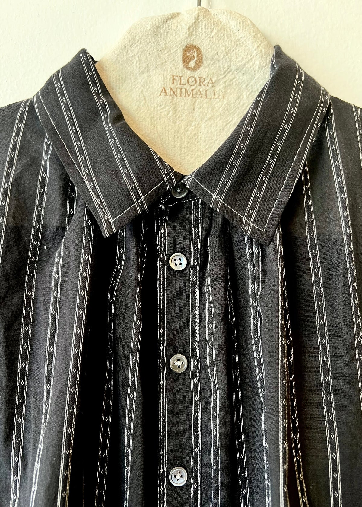 collar closeup of black shirt with white stripes on a hanger with flora animalia logo