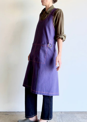Model wearing Flora Animalia organic canvas harvest apron in purple grape, pocket and hardware detail, side view.