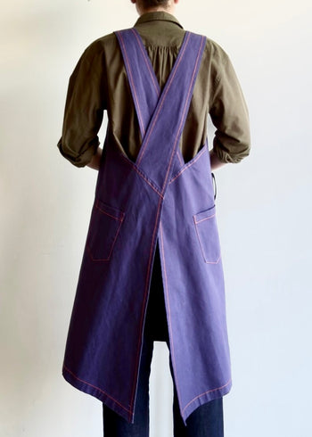 Model wearing Flora Animalia organic canvas harvest apron in purple grape, back view showing cross-back straps.