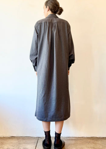 Rear view of a person wearing a long dark gray shirt dress against a plain background