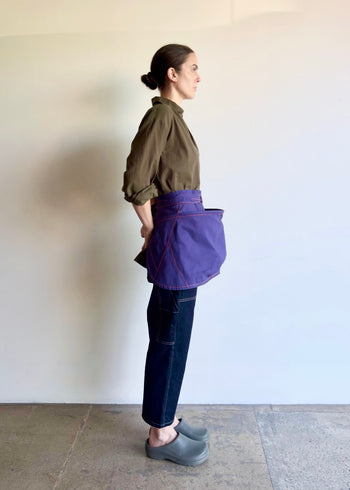 Model wearing Flora Animalia organic canvas basket apron in purple grape, side view.