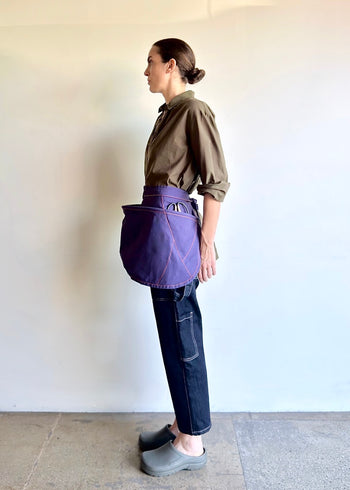 Model wearing Flora Animalia organic canvas basket apron in purple grape, side view.