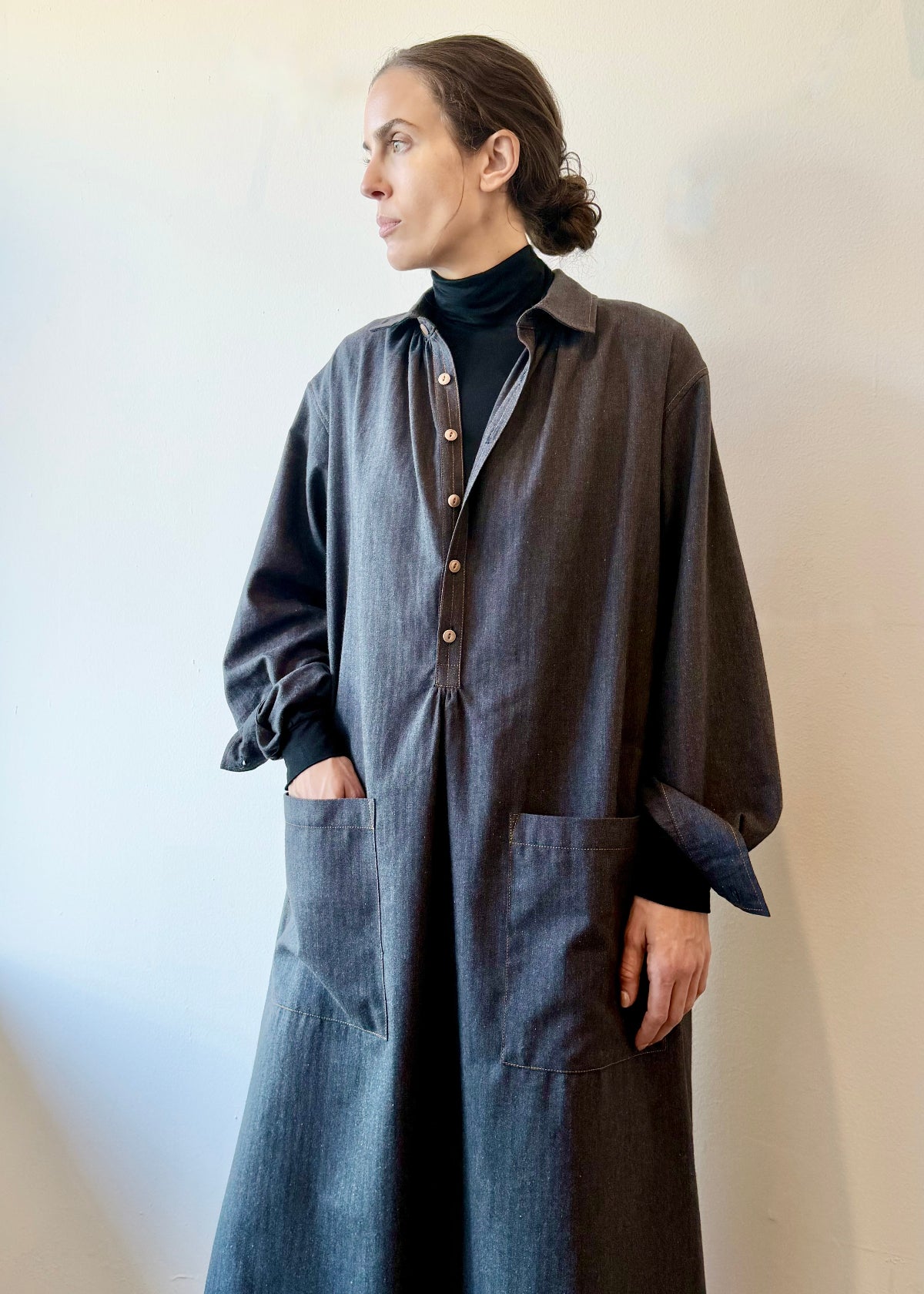 Woman wearing a long dark flannel dress with hand in pocket, against a plain background