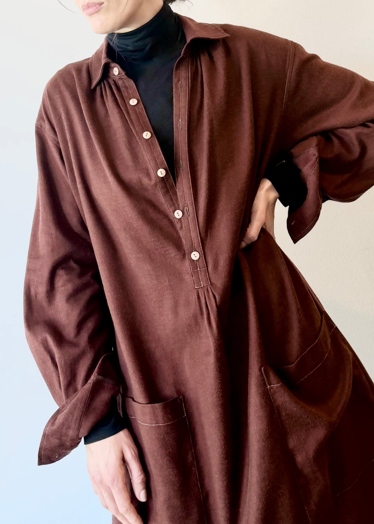Burgundy shirt dress with buttons and a black turtleneck underneath worn by a person on a plain background