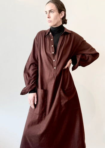 Woman wearing a wine colored dress over a black turtleneck against a plain background with hand on waist.