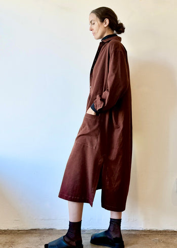 Person wearing a long maroon dress against a plain wall.