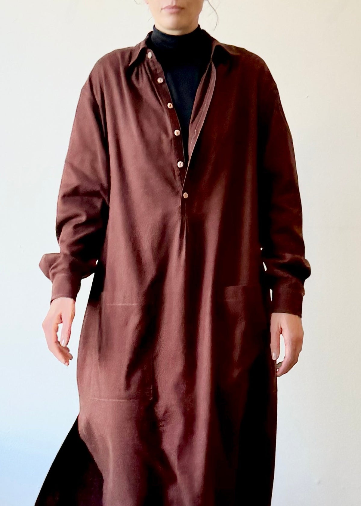 Person wearing a long maroon dress over a black turtleneck against a white background