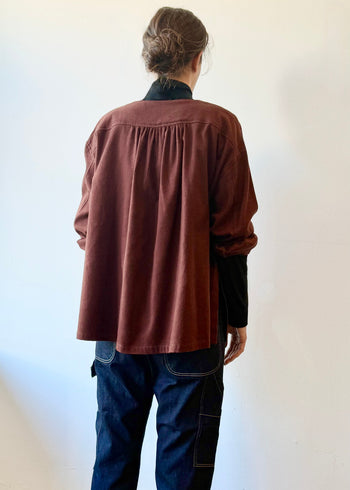 Rear view of person wearing a burgundy shirt and dark pants against a white wall