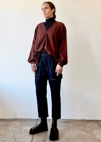 Person wearing a maroon colored v-neck shirt over a black turtleneck with dark jeans against a white wall.