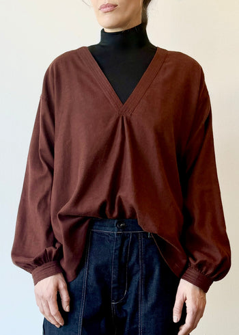 Person wearing a brick red blouse over a black turtleneck with blue jeans on a plain background