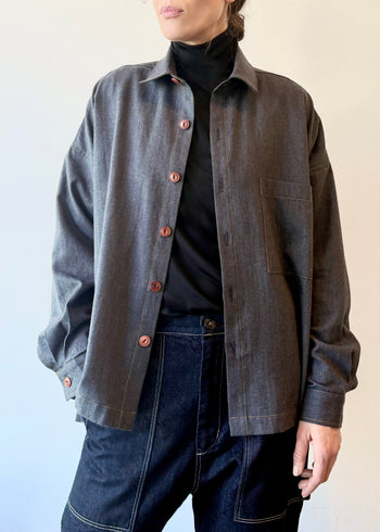 Person wearing a slate blue button-up shirt over a black turtleneck with blue jeans against a light background