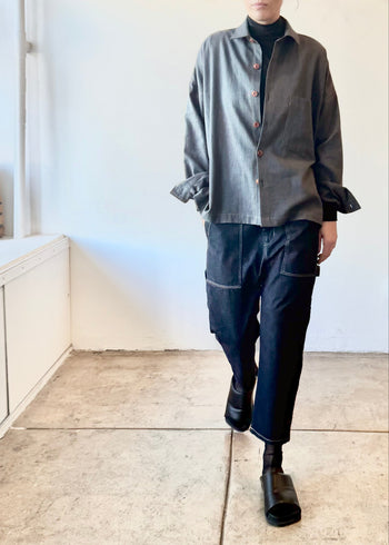 Person wearing a steel colored shirt over a black turtleneck and dark denim pants in a minimal indoor setting