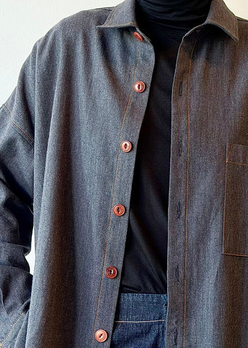 Person wearing a steel blue flannel shirt with luggage colored buttons over a black turtleneck on a plain background