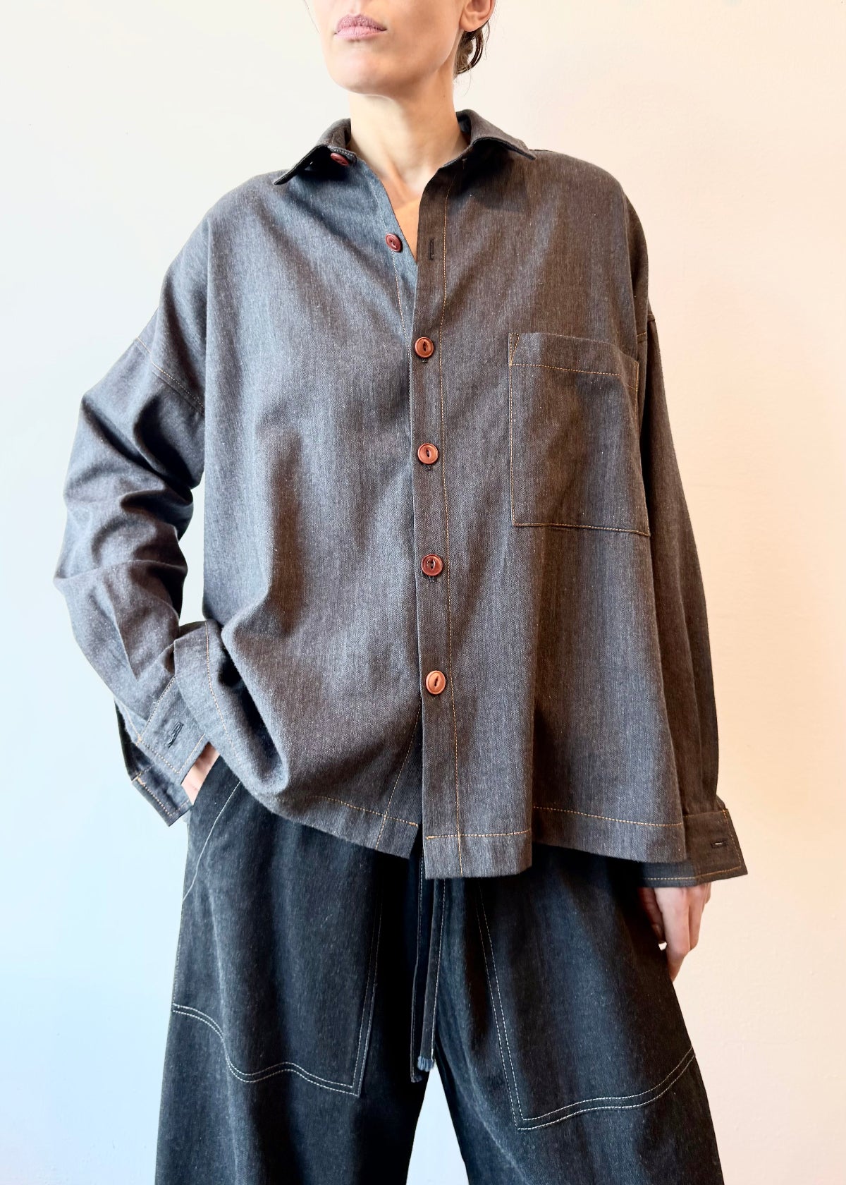 Person wearing a blue flannel shirt with brown buttons and one pocket with dark drawstring picker's  pants on a gradient background