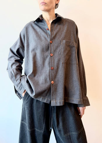 Person wearing a blue flannel shirt with brown buttons and one pocket with dark drawstring picker's  pants on a gradient background