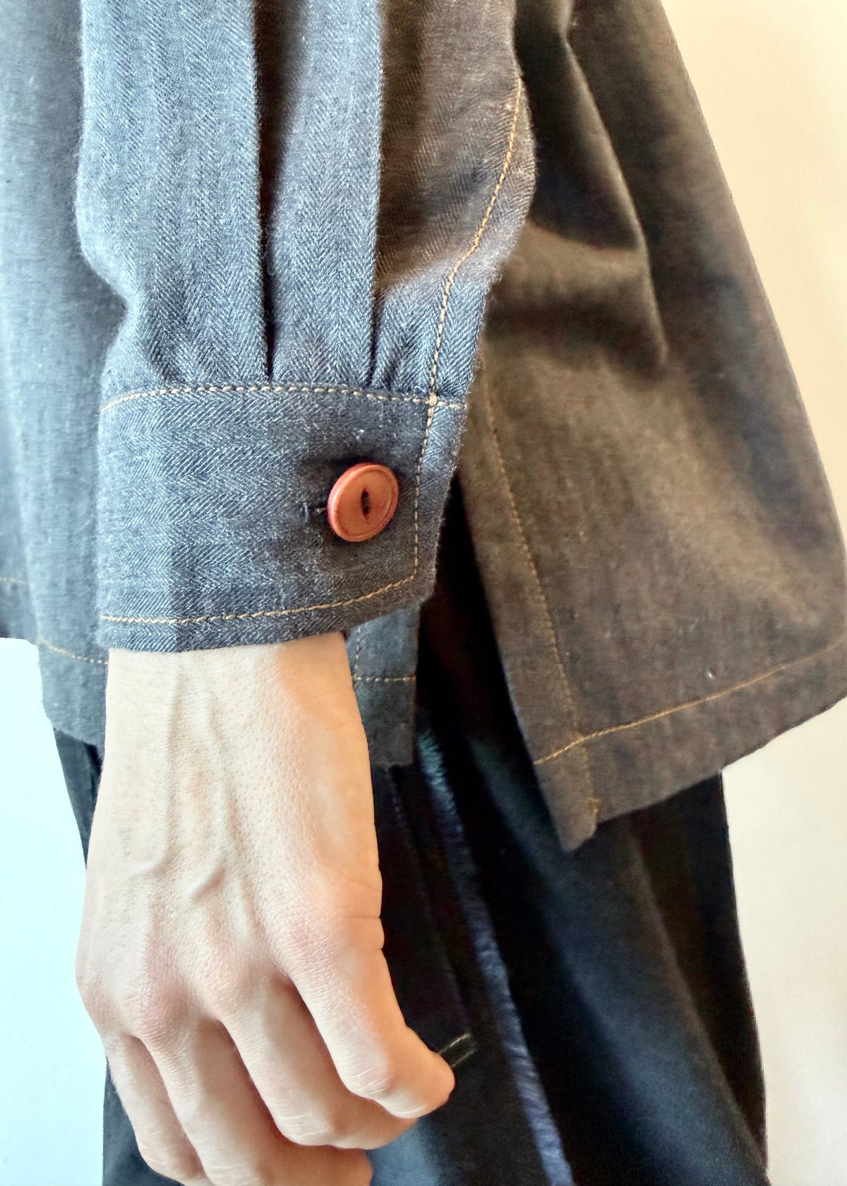 Close-up of a cuff with brown button and hem of a blue gray colored flannel and contrasting stitching