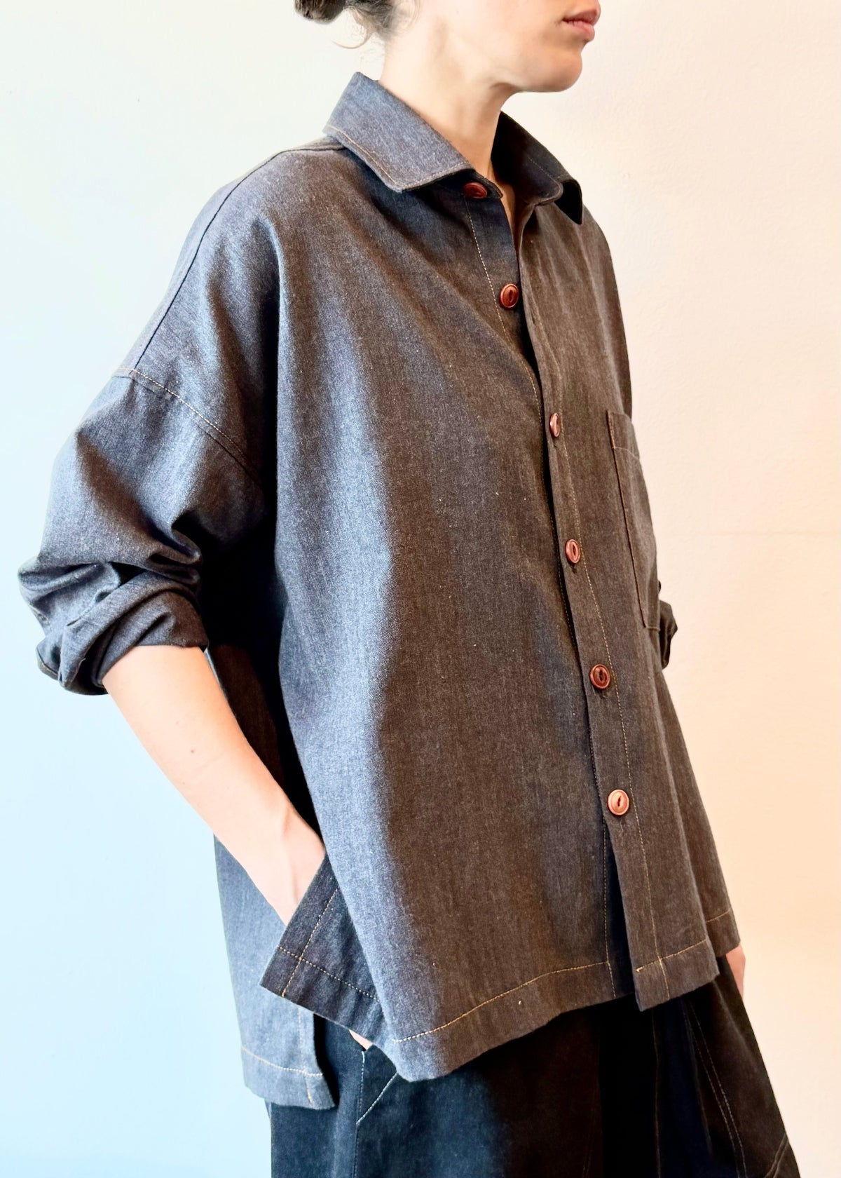 Person wearing a dark blue flannel shirt with herringbone texture and brown buttons on a light background