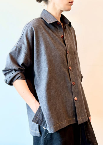 Person wearing a dark blue flannel shirt with herringbone texture and brown buttons on a light background