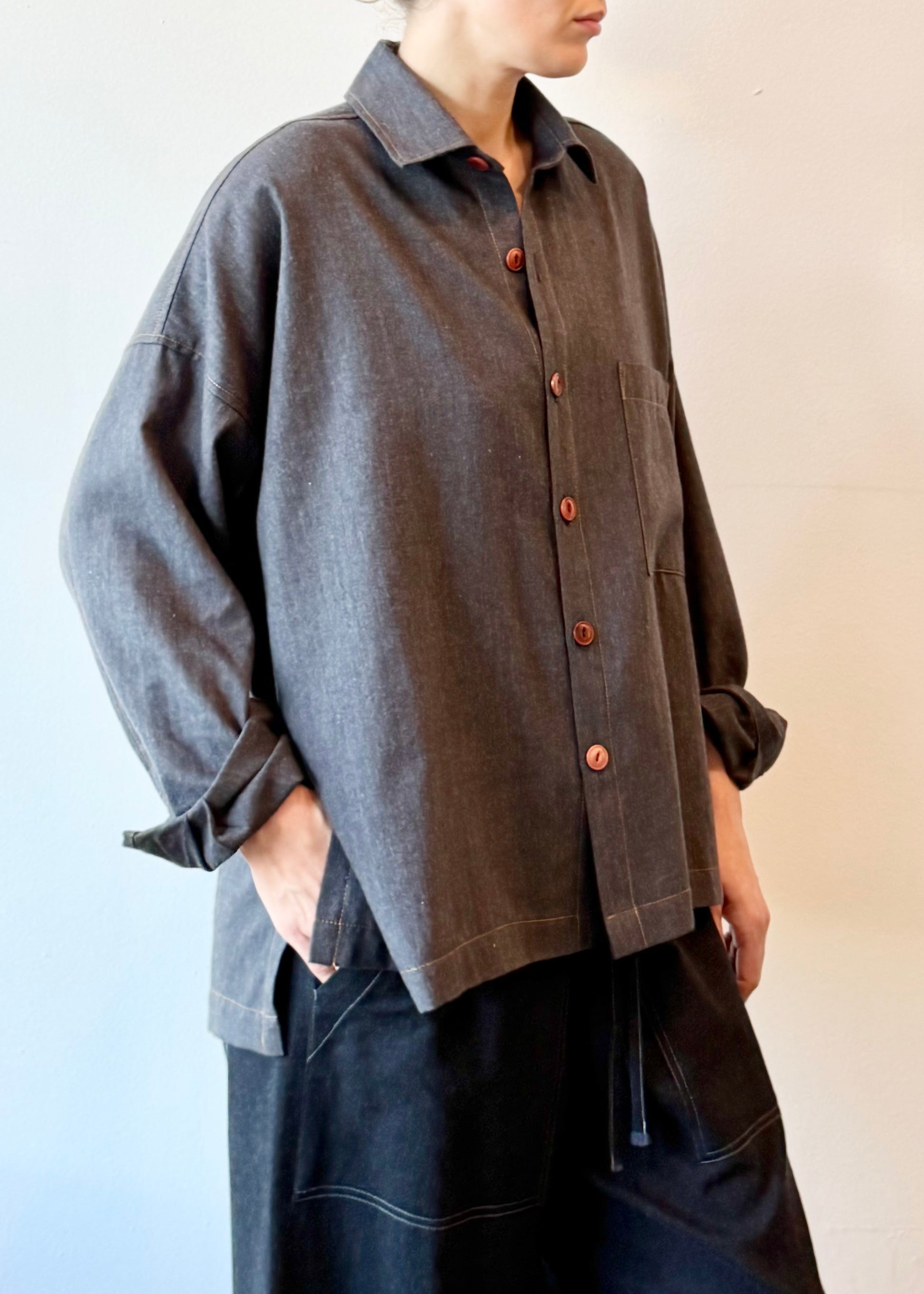 Woman wearing a blue gray button-up shirt with brown buttons against a plain background