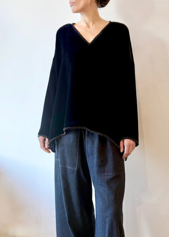 Model wearing a navy blue velvet Praia tunic with long sleeves and a V-neckline  and gray pants against a plain background.