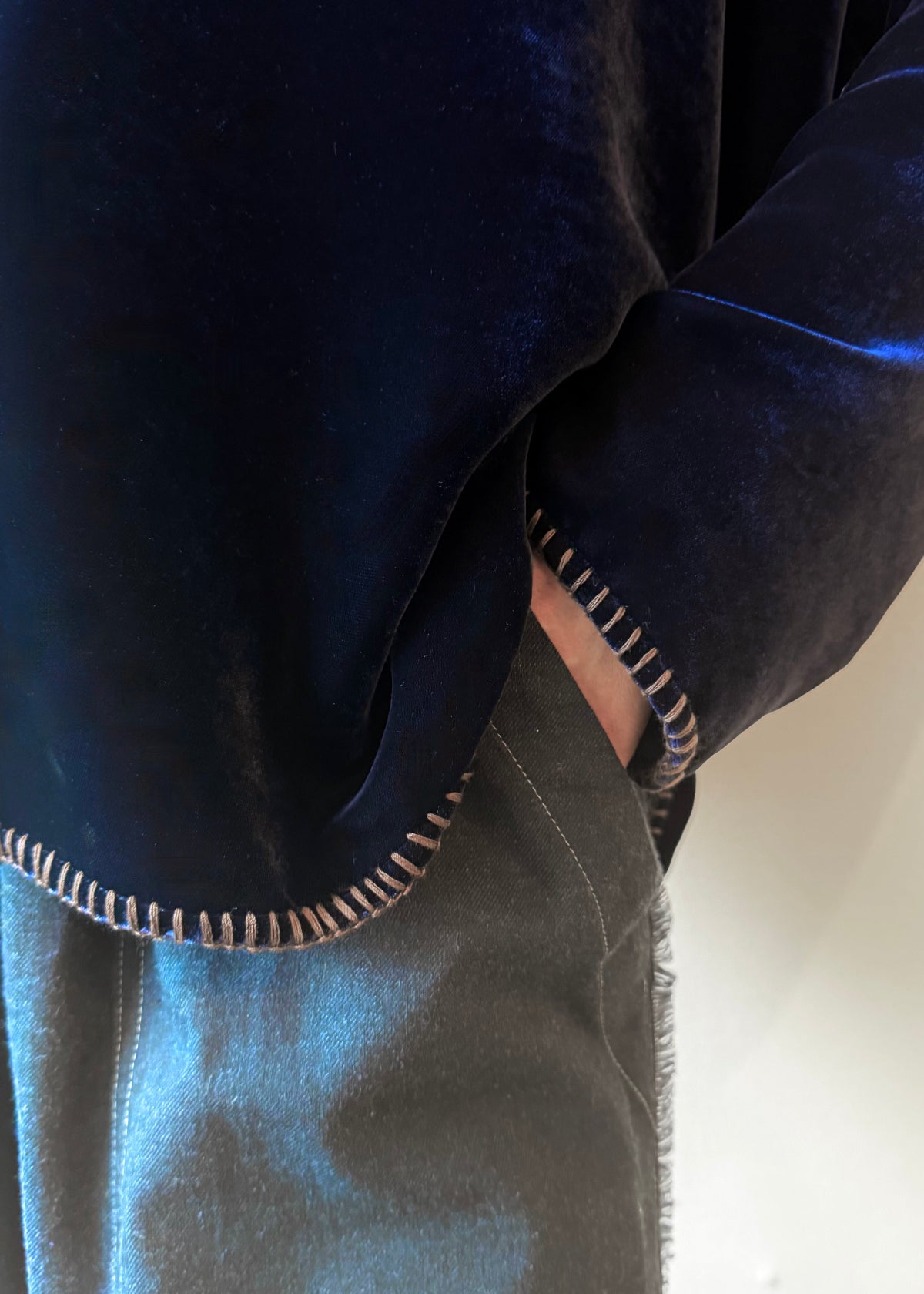 Close-up of sleeve and hem with almond color contrast stitching on a person wearing a dark blue velvet top against a light background.