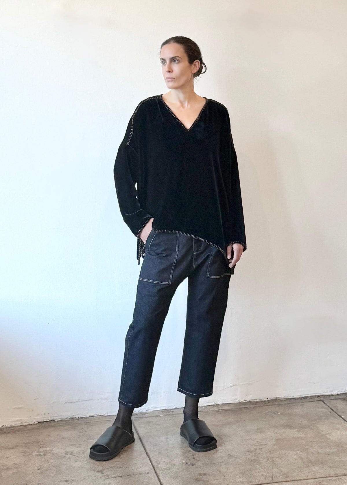 Person wearing a navy velvet shirt and dark denim jeans standing against a plain white wall.