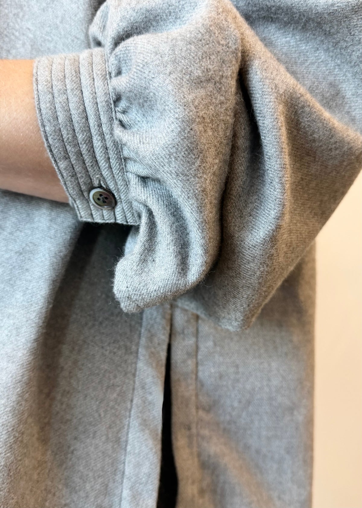 Close-up of a gray flannel shirt with pushed-up sleeve and button detail.