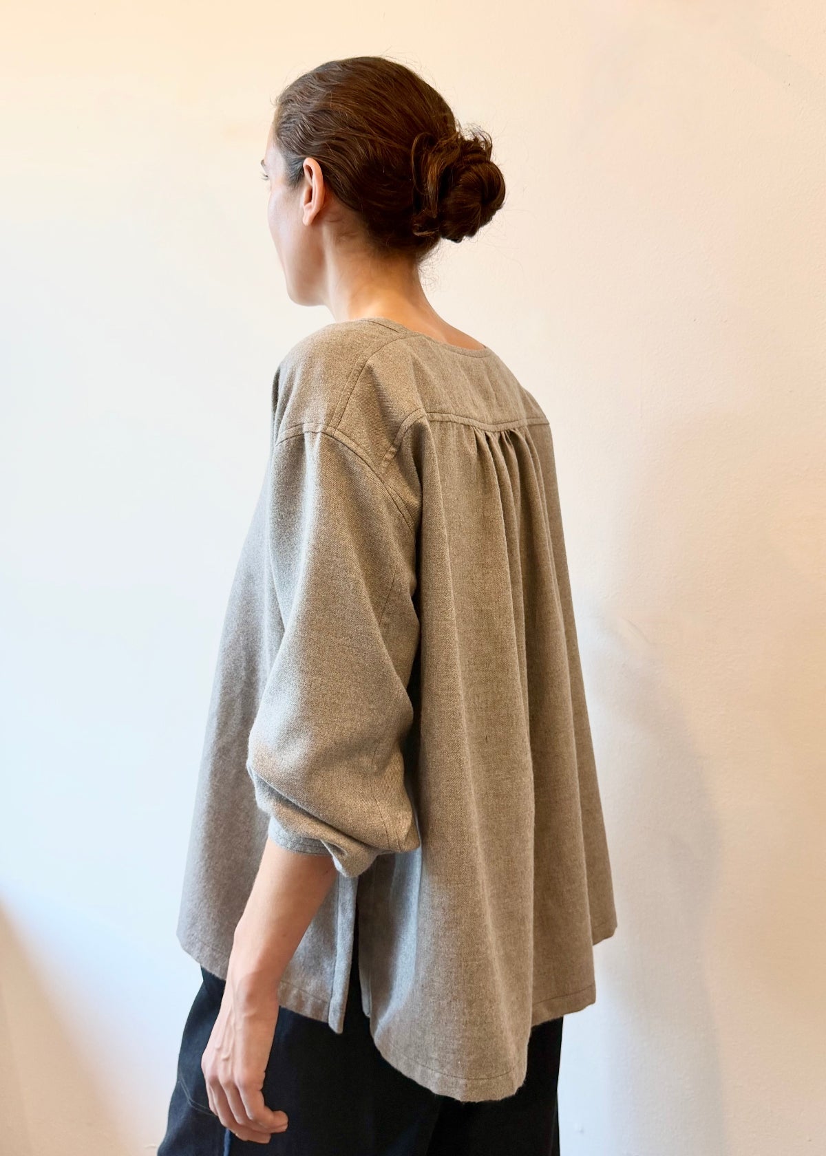 Rear view of a person wearing a light gray blouse against a plain background