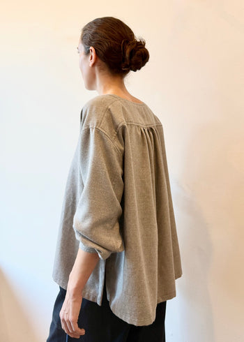 Rear view of a person wearing a light gray blouse against a plain background