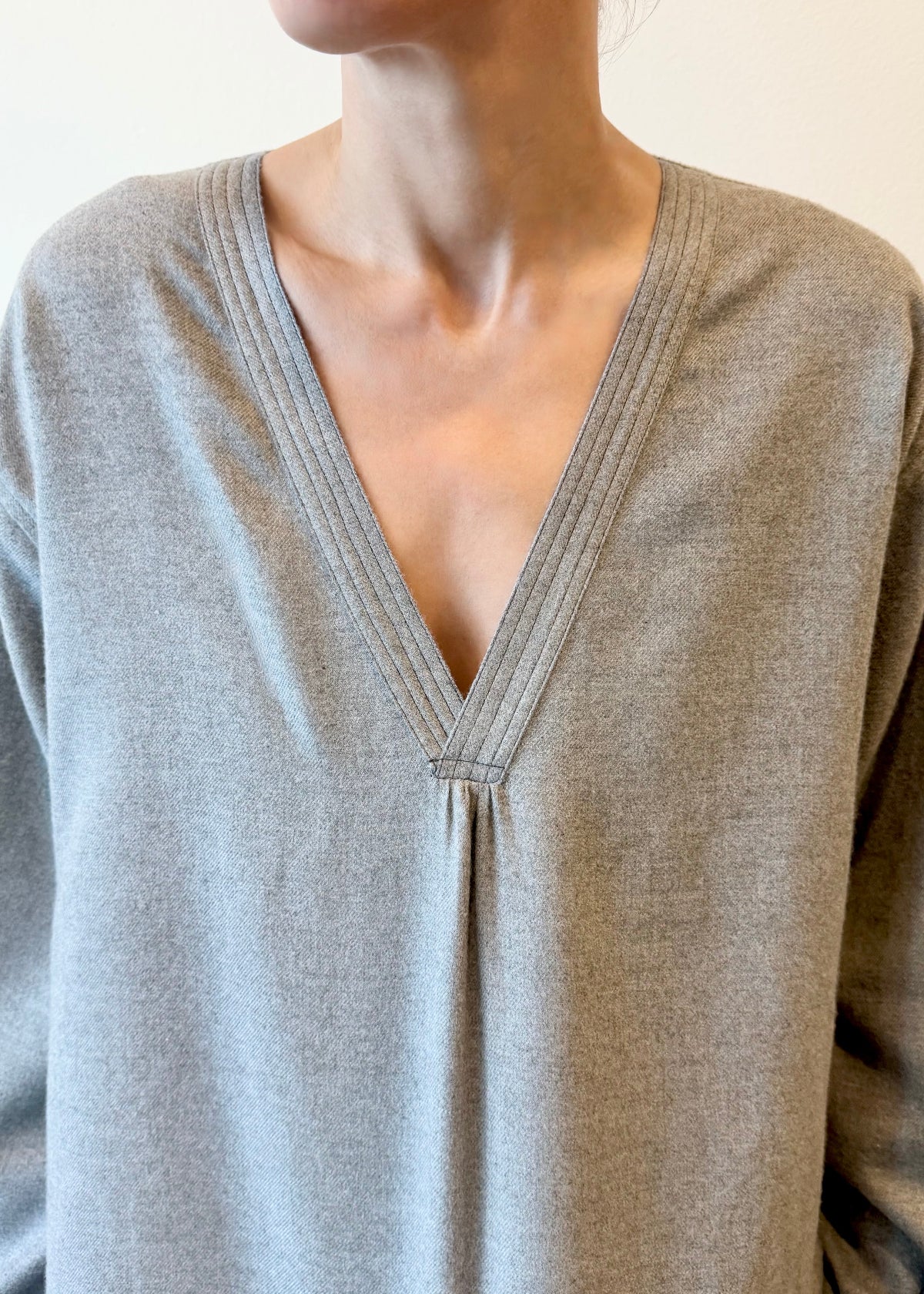 Close-up of a person wearing a light gray long-sleeve shirt with a V-neck.