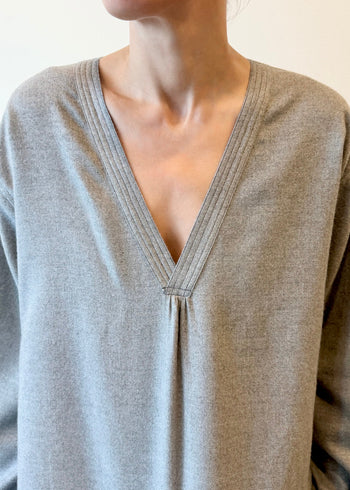 Close-up of a person wearing a light gray long-sleeve shirt with a V-neck.