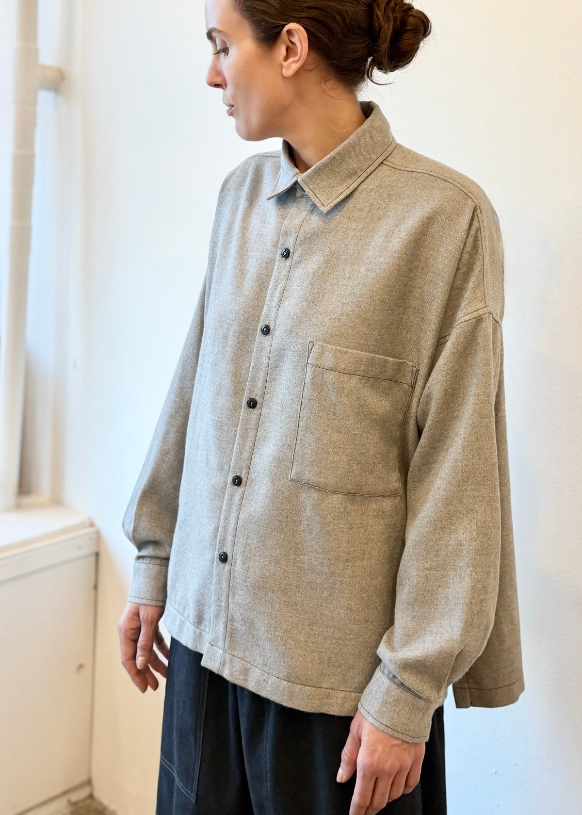 Person wearing a light gray button-up shirt with black buttons against a white wall