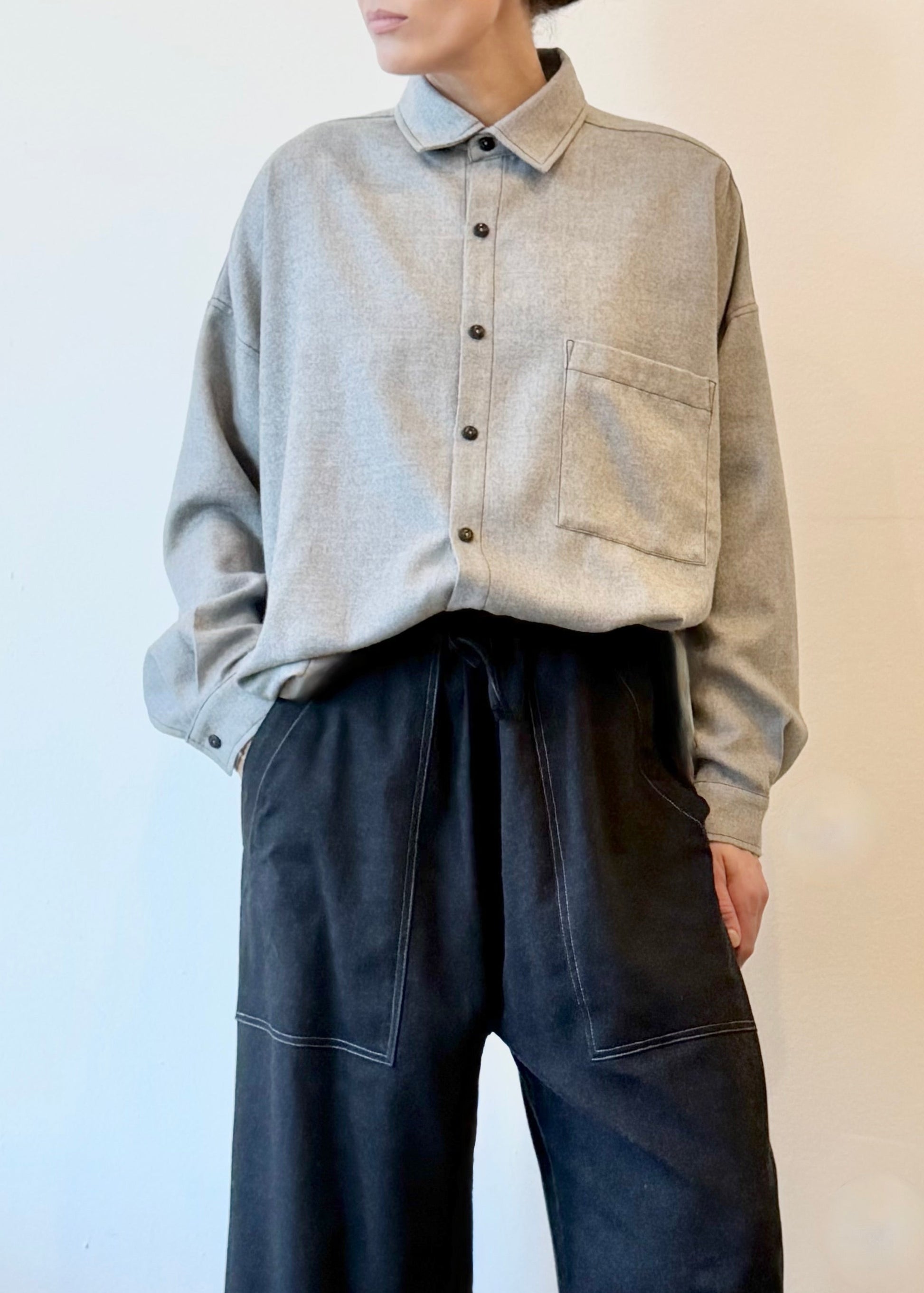 Person wearing a light gray shirt and dark drawstring pants against a plain background