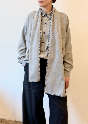 Person wearing a light gray button shirt with a light gray scarf over their shoulders with a plain background