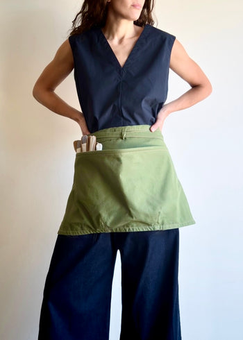 Model wearing Flora Animalia organic canvas basket apron in grass green, front view.