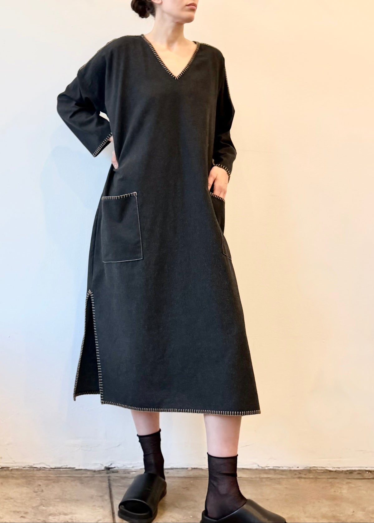 Woman wearing a dark gray dress with pockets and blanket stitching against a plain background