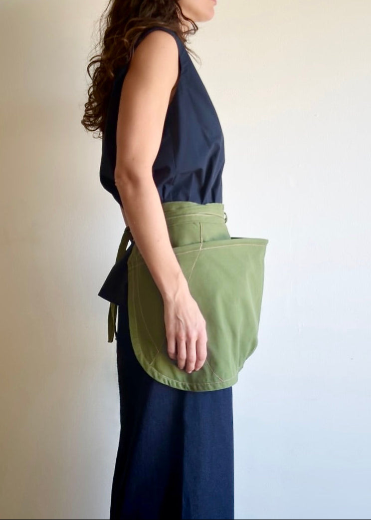Model wearing Flora Animalia organic canvas basket apron in grass green, side view.