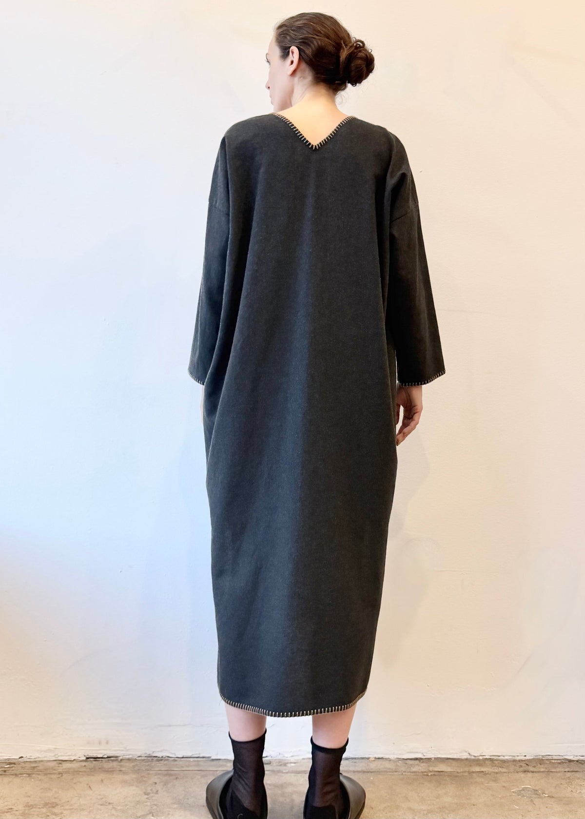 Rear view of person wearing a long dark gray dress against a plain background