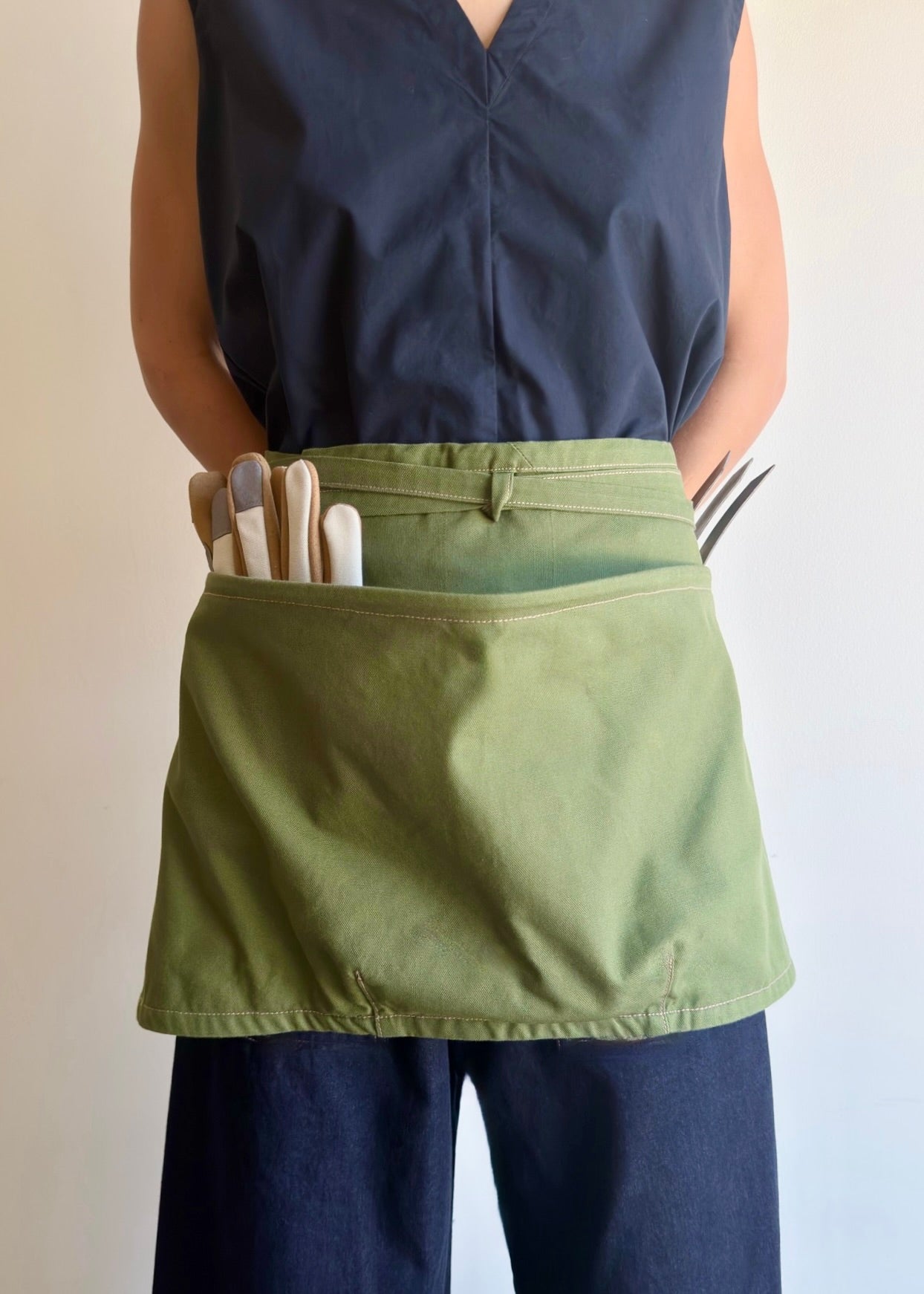 Model wearing Flora Animalia organic canvas basket apron in grass green, front view.