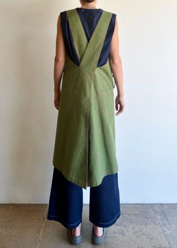 Model wearing Flora Animalia organic canvas harvest apron in grass green, back view showing cross-back straps.
